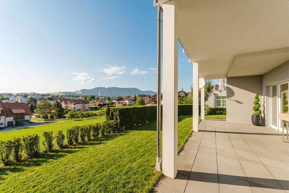 Große überdachte Terrasse mit Fliesenboden und weitem Blick über den Garten und die Umgebung.