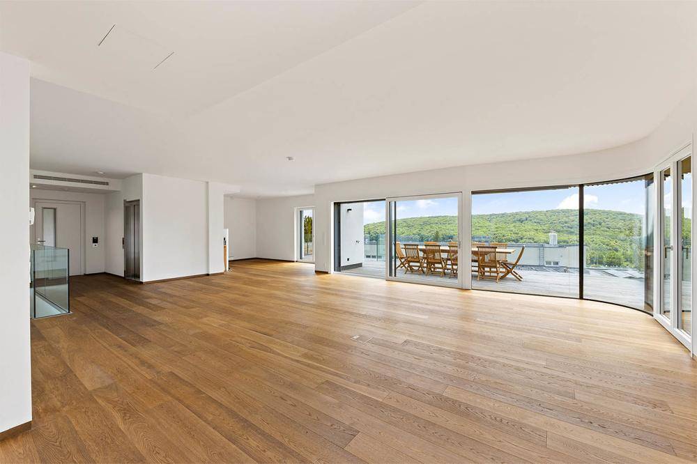 Geräumiges, helles Wohnzimmer mit Holzboden und Zugang zu einer großen Terrasse mit Weitblick.
