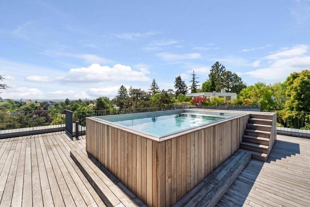 Dachpool mit Holzverkleidung und umlaufender Terrasse, umgeben von Grün und Weitblick.