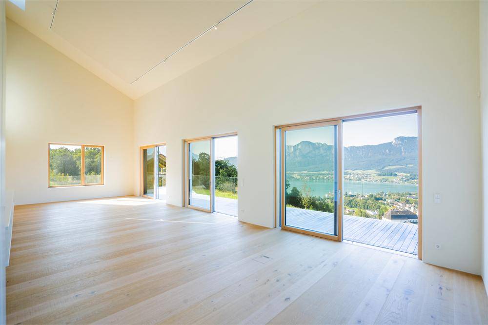 Heller, leerer Wohnraum mit hohen Decken, Holzboden und großen Schiebetüren mit Seeblick.
