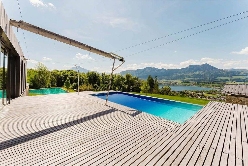 Großzügige Holzterrasse mit Infinity-Pool und atemberaubendem Blick auf den See und die Berge.