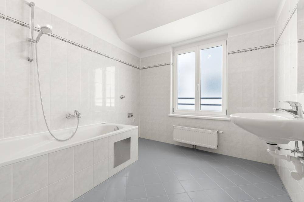 Helles Badezimmer mit Badewanne, Duschvorrichtung, Waschbecken und Fenster für natürliche Belüftung.