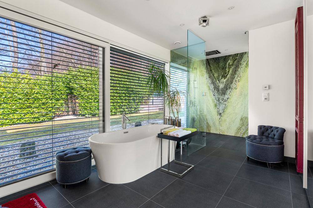 Luxuriöses Badezimmer mit freistehender Badewanne, großer Fensterfront und grüner Marmorwand.