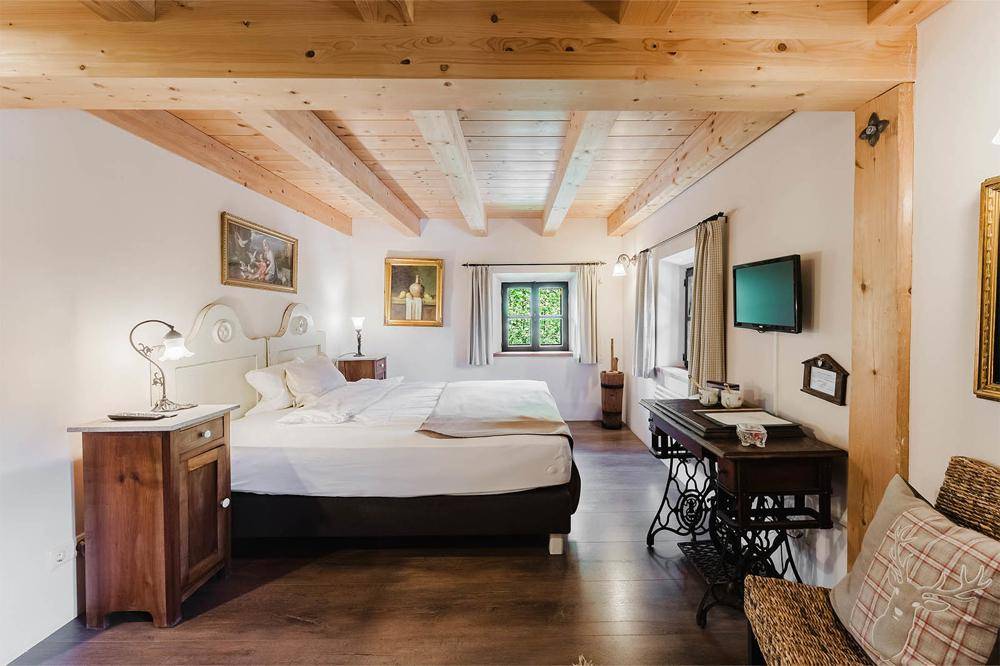 Helles Schlafzimmer mit Holzbalkendecke, Doppelbett und rustikalen Möbeln im Landhausstil.