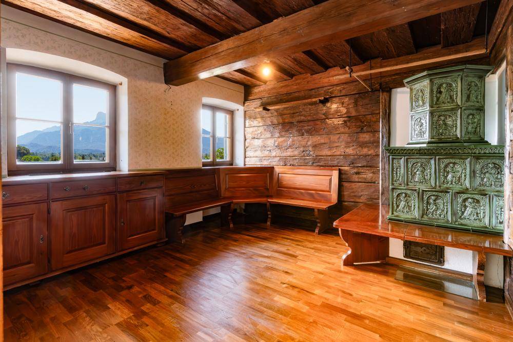 Rustikaler Raum mit Holzbalkendecke, Holzwänden, eingebauten Bänken und einem traditionellen Kachelofen.