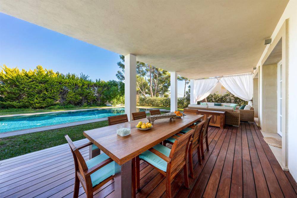 Geräumige überdachte Terrasse mit Esstisch und Lounge-Bereich, direkt am Pool gelegen und von Grün umgeben.
