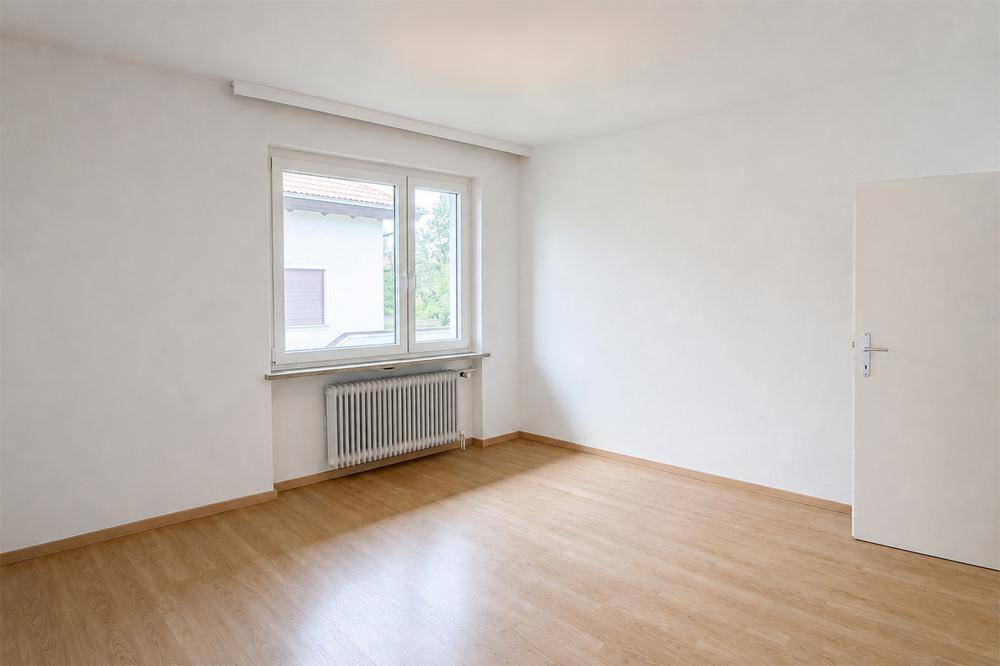 Schlichtes Zimmer mit hellem Parkettboden und großem Fenster, ideal als Schlaf- oder Arbeitszimmer.