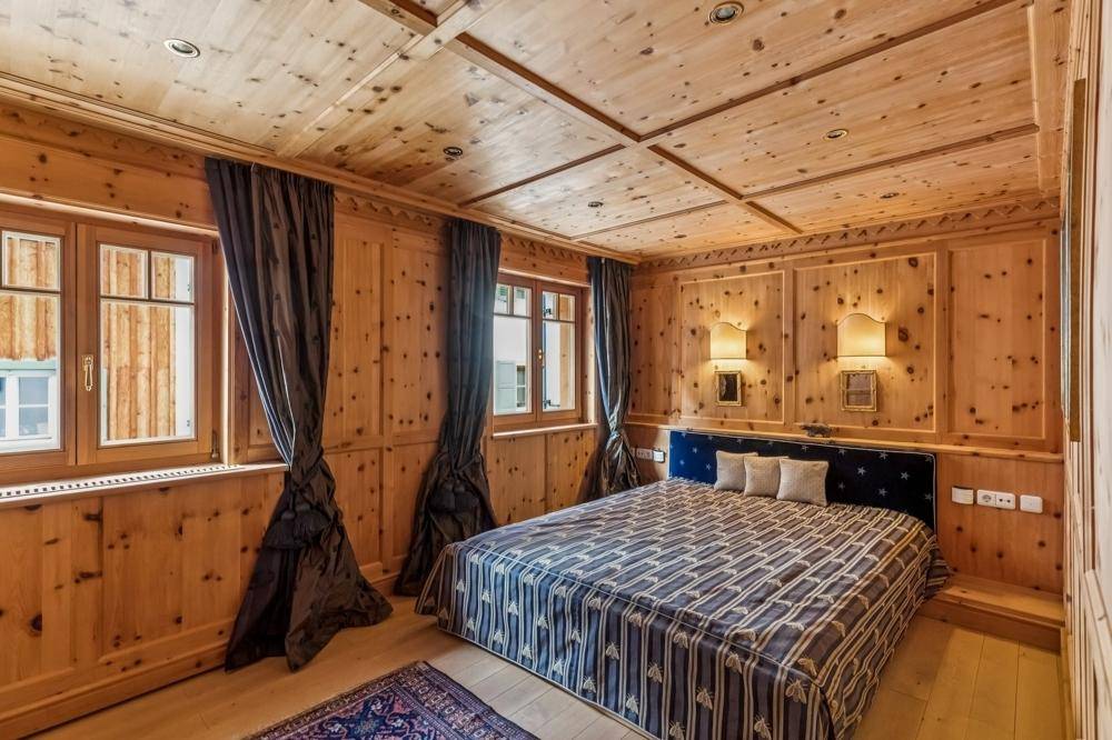 Schlafzimmer im alpinen Stil mit Holzvertäfelung, Doppelbett und traditionellen Wandleuchten.