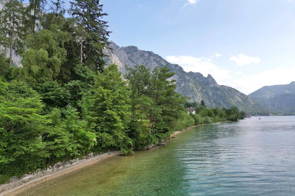 Malerische Landschaft mit klarem See, bewaldeten Ufern und majestätischen Bergen im Hintergrund.