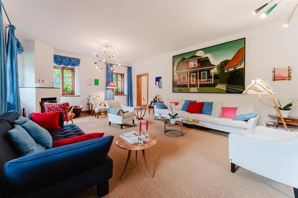 Helles und farbenfrohes Wohnzimmer mit mehreren Sitzbereichen, Teppichboden und großer Kunst an der Wand.