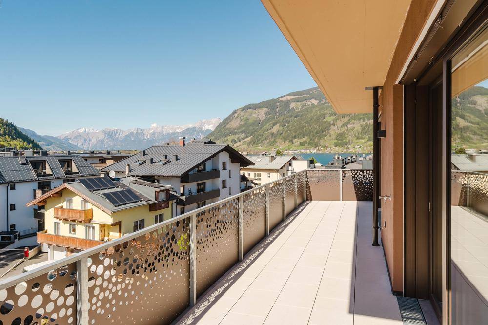 Geräumiger Balkon mit modernem, perforiertem Geländer und weitem Blick auf den See und die Berge.