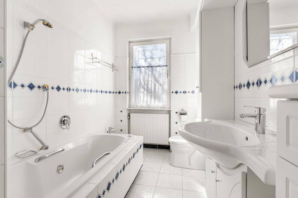 Badezimmer mit weiß-blauen Fliesen, Badewanne, Waschbecken und Fenster für Tageslicht.