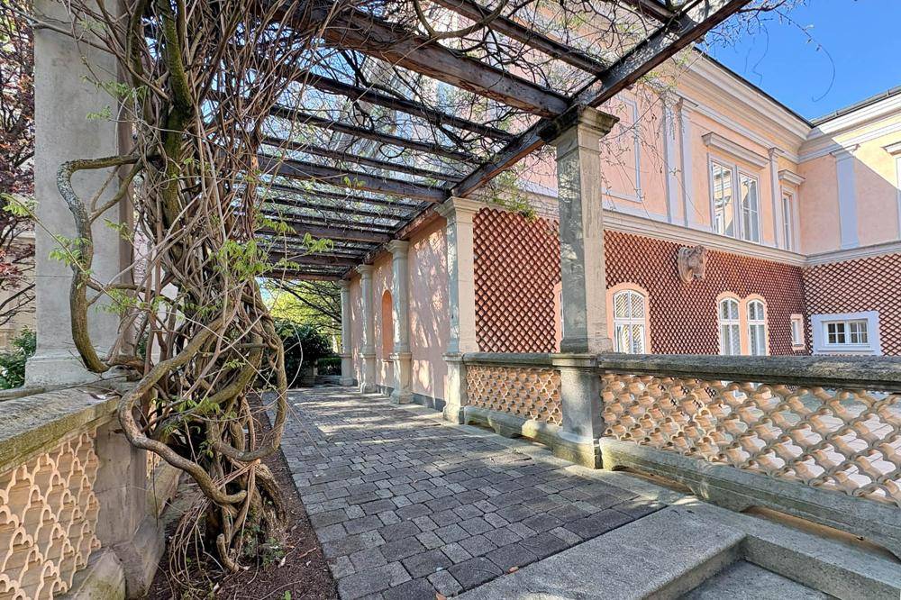 Überdachter Gang mit Pergola und Steinpflaster im historischen Gartenbereich der Liegenschaft.