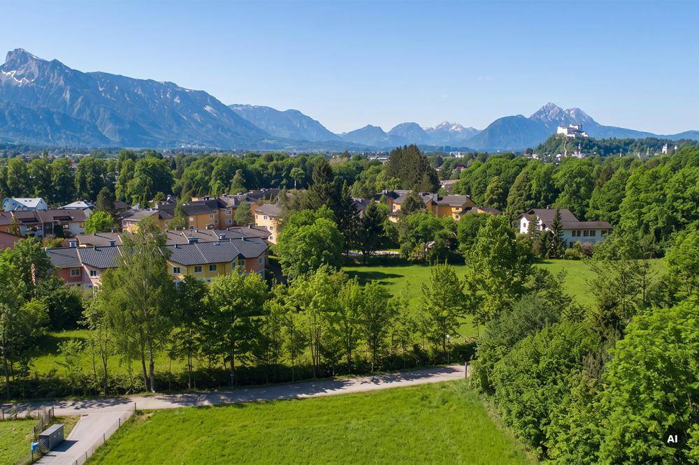 Panoramablick über eine grüne Wohnsiedlung mit vielen Bäumen und majestätischen Bergen im Hintergrund, inklusive einer Burg.