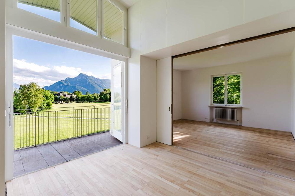 Heller Wohnraum mit Holzboden, Zugang zum Balkon und weitem Bergblick.