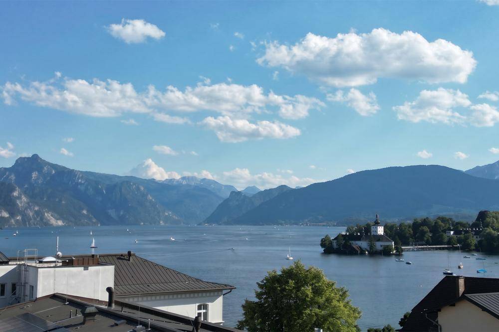 Panoramablick auf den See mit Bergen und einem Schloss auf einer Insel unter blauem Himmel.