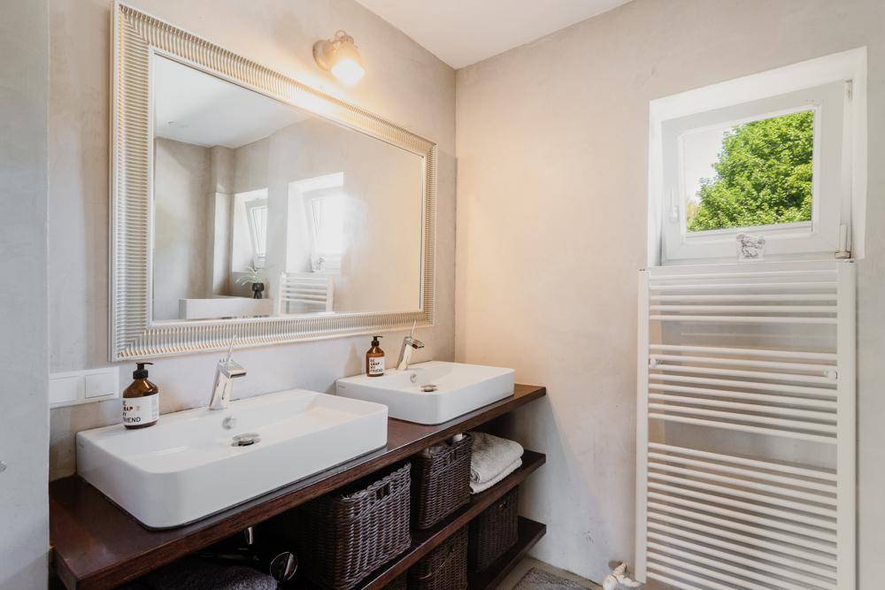 Modernes Badezimmer mit Doppelwaschbecken, großem Spiegel, beheiztem Handtuchhalter und Fenster.