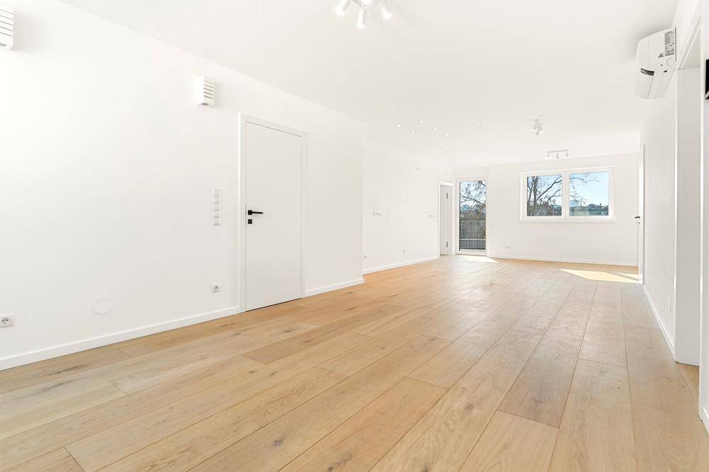 Helles, leeres Wohnzimmer mit neuem Holzparkettboden und weißen Wänden, bereit zum Einzug.