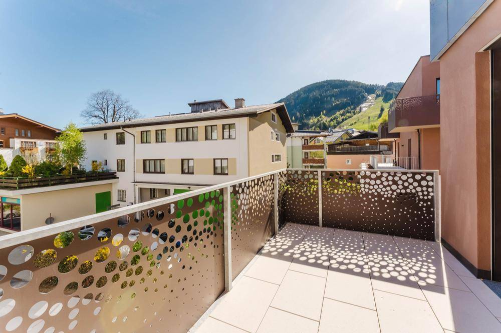 Kleiner Balkon mit moderner Lochblechbrüstung und Blick auf die Nachbarschaft und Berge.
