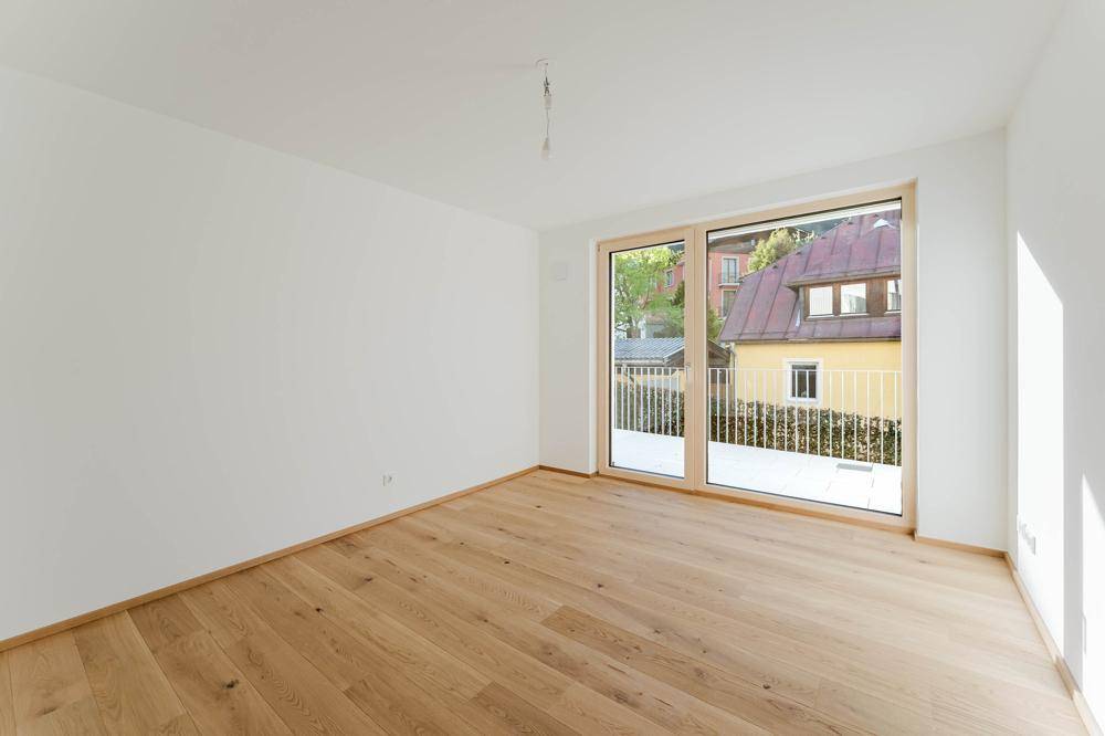 Helles Schlafzimmer mit Holzboden und großem Fenster, das einen französischen Balkon bildet.