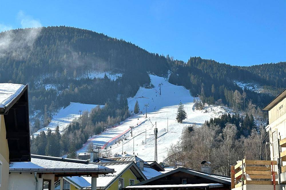Blick auf eine schneebedeckte Skipiste mit Liftanlagen und bewaldeten Bergen im Hintergrund.