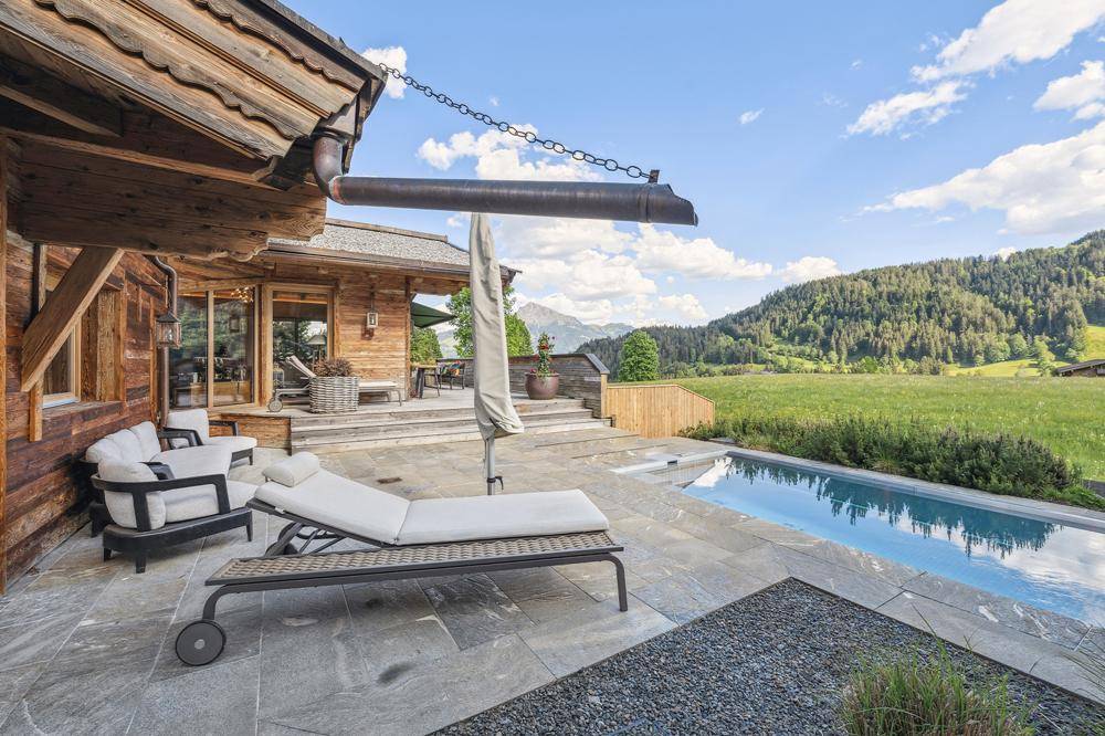 Sonnige Terrasse mit Pool, Liegestühlen und weitem Blick über die grüne Hügellandschaft.