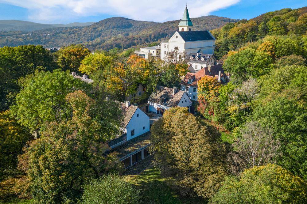 Malerische Luftaufnahme eines Dorfes mit Kirche auf einem Hügel, umgeben von Wäldern und Bergen.