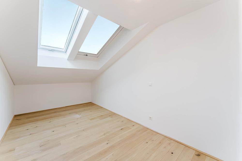 Helles Zimmer mit Holzboden, schrägen Wänden und zwei großen Dachfenstern.