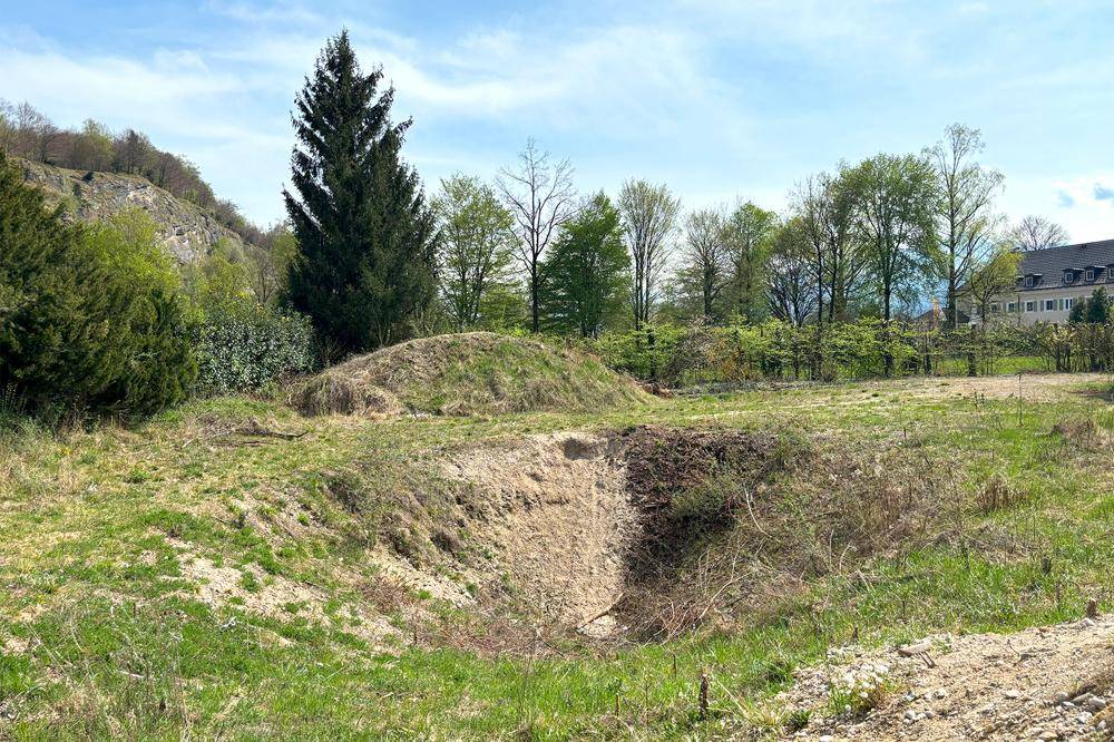 Weitläufiges Grundstück mit natürlicher Vegetation, Hügeln und einem Gebäude in der Ferne.