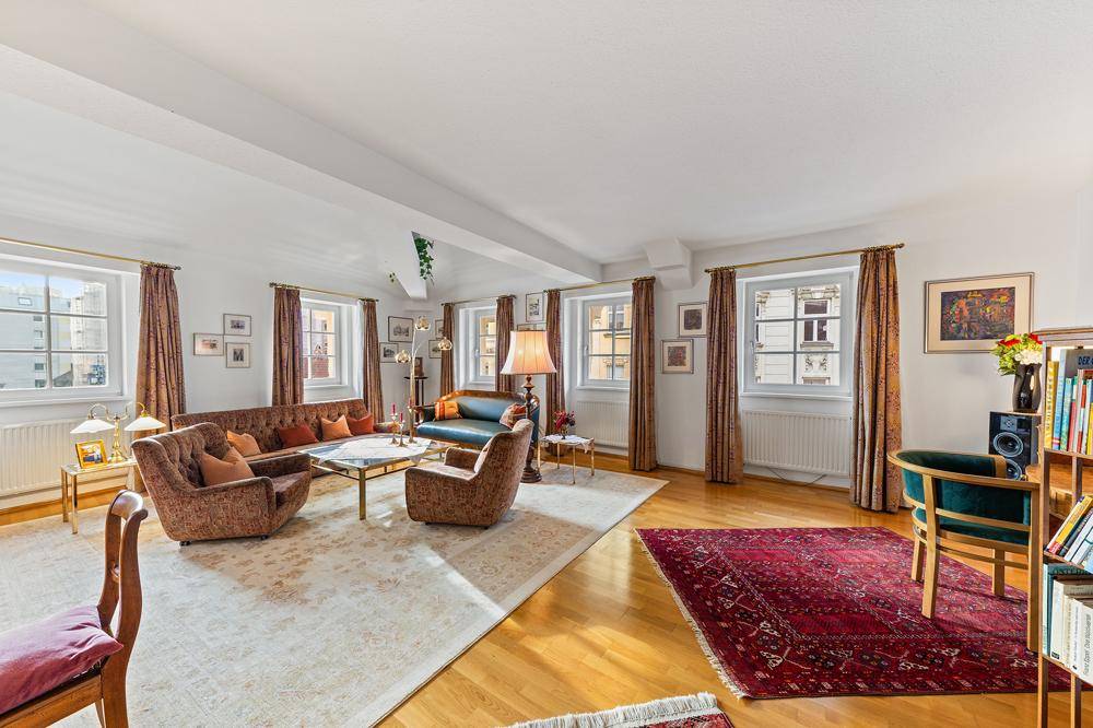 Helles Wohnzimmer mit mehreren Fenstern, bequemen Sofas und traditionellen Teppichen.