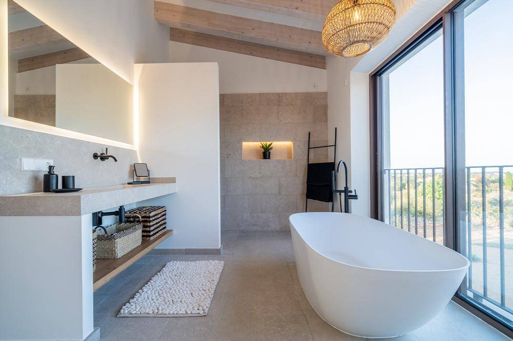 Luxuriöses Badezimmer mit freistehender Badewanne, Doppelwaschbecken und raumhohem Fenster mit Aussicht.