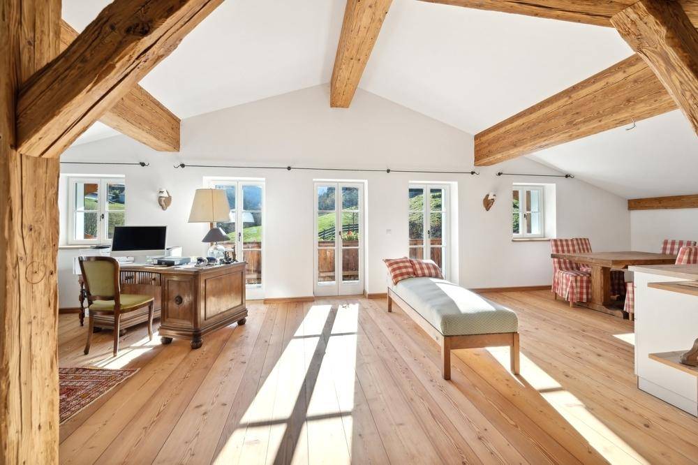 Helles Dachgeschosszimmer mit hohen Decken, sichtbaren Holzbalken und Zugang zu einem Balkon.