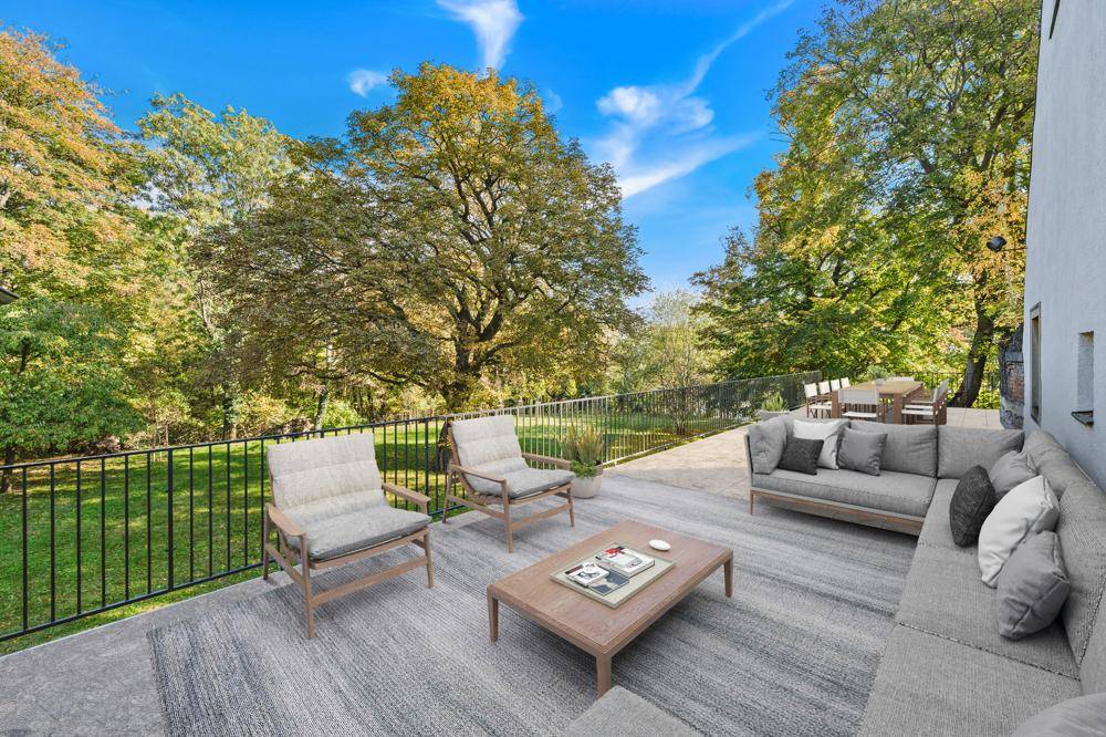 Große Terrasse mit modernen Loungemöbeln, umgeben von üppigem Grün und hohen Bäumen.