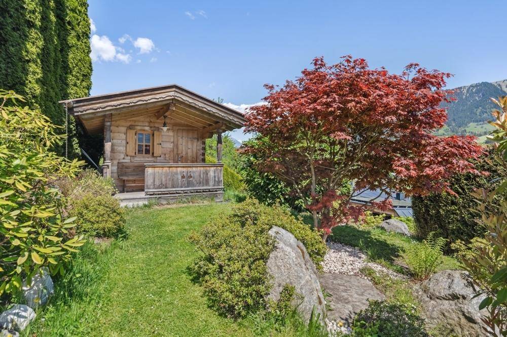 Idyllischer Gartenbereich mit einem kleinen Holzhaus, Felsen und einem roten Ahornbaum.
