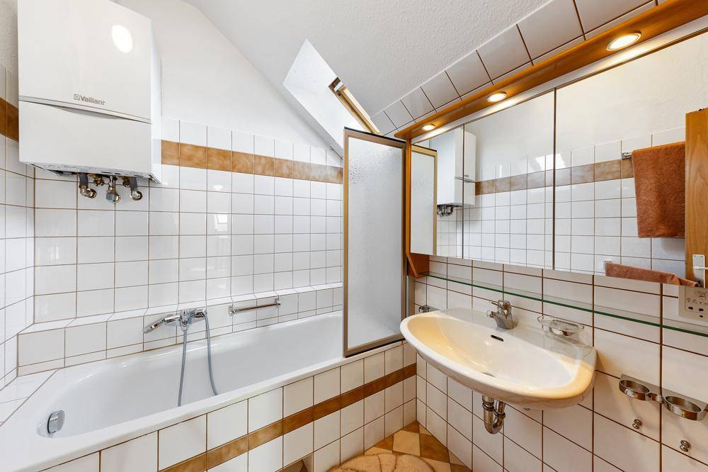 Helles Badezimmer mit Badewanne, Waschbecken und Wandfliesen in Weiß und Braun.