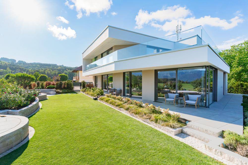 Elegantes modernes Haus mit weitläufigem Rasen und gepflegter Gartenanlage unter blauem Himmel.
