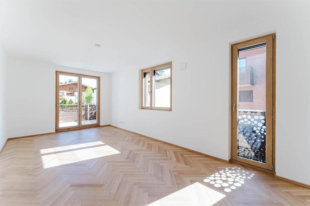 Heller Raum mit Fischgrätparkett, großen Fenstern und Zugang zu einem französischen Balkon.