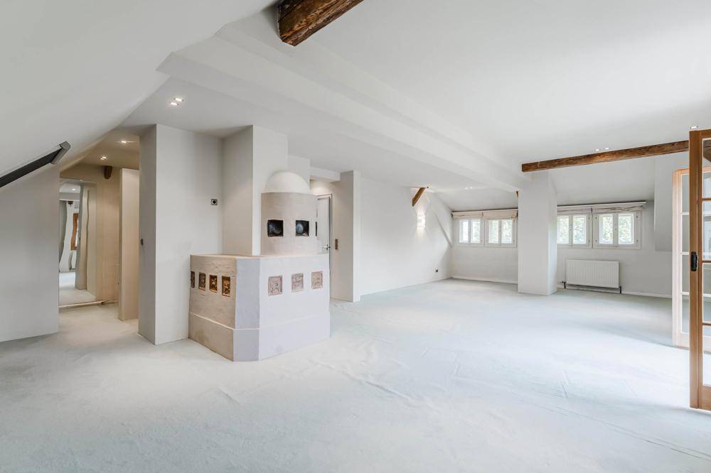 Geräumiger Wohnbereich im Dachgeschoss mit traditionellem Kachelofen und sichtbaren Holzbalken.