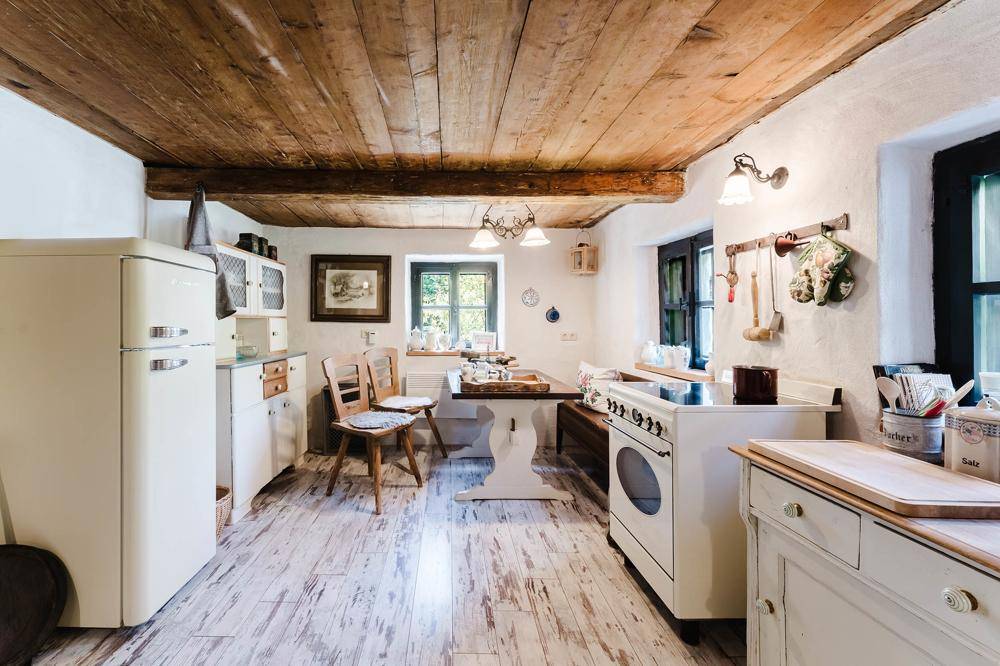 Gemütliche Küche im Landhausstil mit Holzbalkendecke, Vintage-Geräten und kleinem Essbereich.