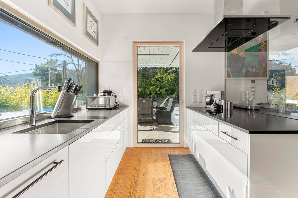 Moderne Küche mit weißen Hochglanzfronten, großem Fenster und Zugang zur Terrasse.