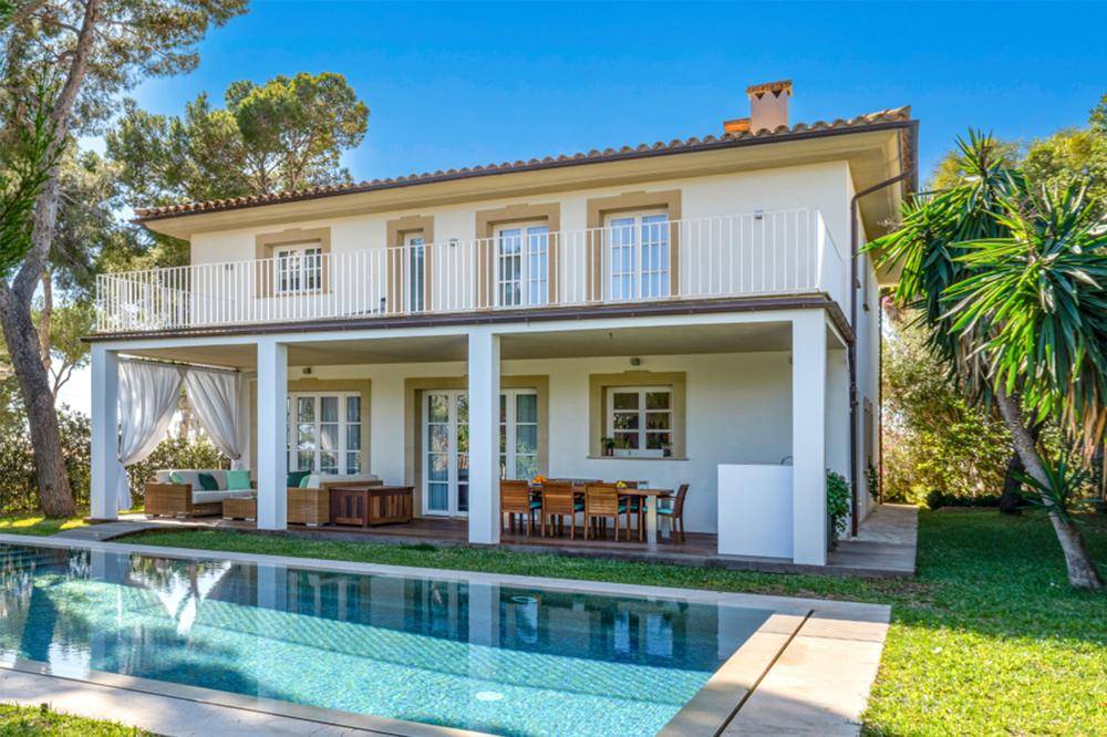 Elegante Villa mit großem Pool und überdachter Terrasse, umgeben von üppigem Grün und hohen Bäumen.