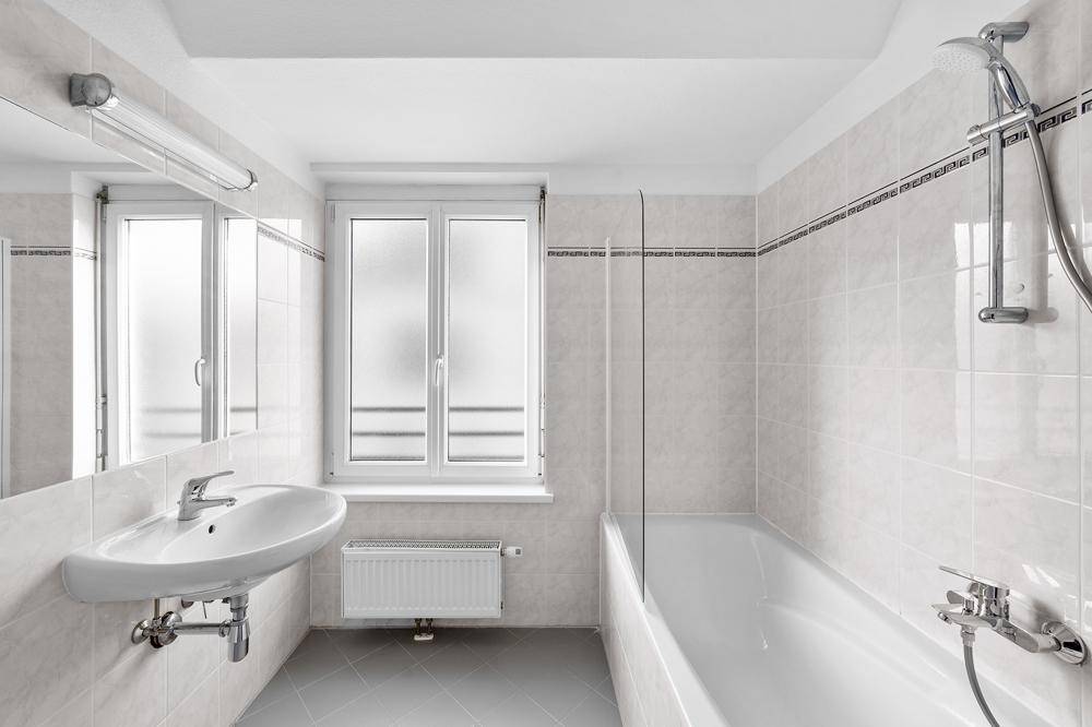 Helles Badezimmer mit Badewanne, Dusche und Fenster, ausgestattet mit hellen Fliesen.