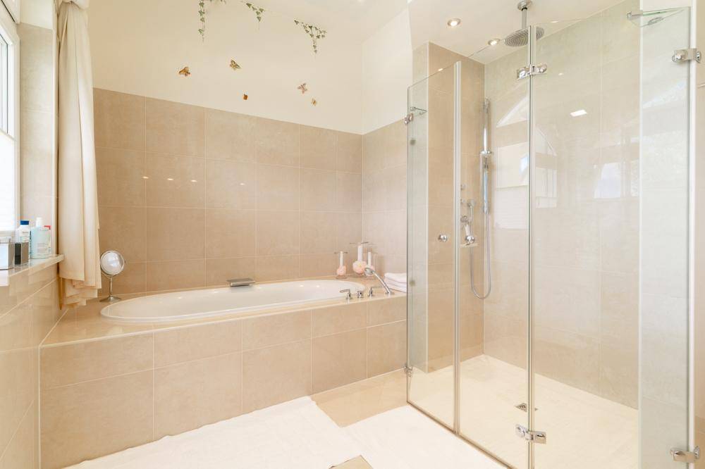 Modernes Badezimmer mit Badewanne, begehbarer Dusche und beigen Fliesen.