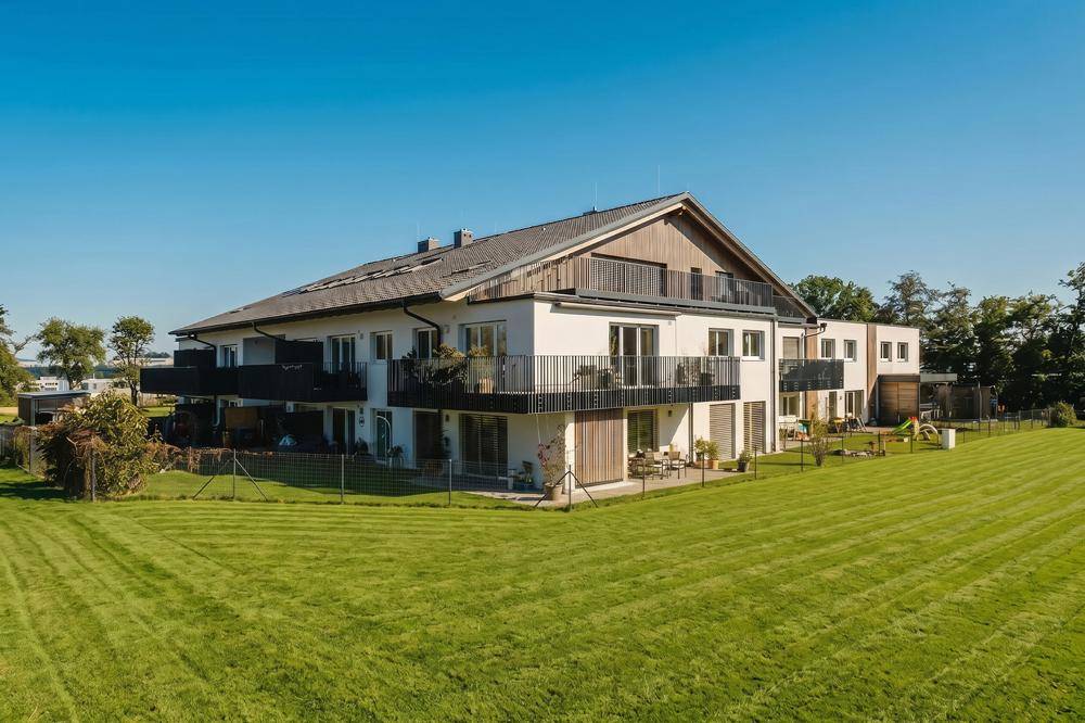 Modernes Mehrfamilienhaus mit großzügigen Grünflächen und Balkonen in ländlicher Umgebung.