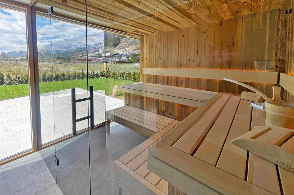 Holzsauna mit großer Glasfront, die einen weiten Blick auf die grüne Landschaft bietet.