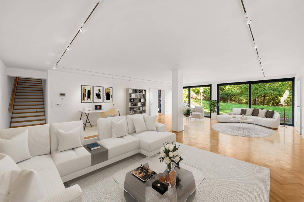 Geräumiges, offenes Wohnzimmer mit weißen Sofas, Parkettboden und großen Fenstern zum Garten.