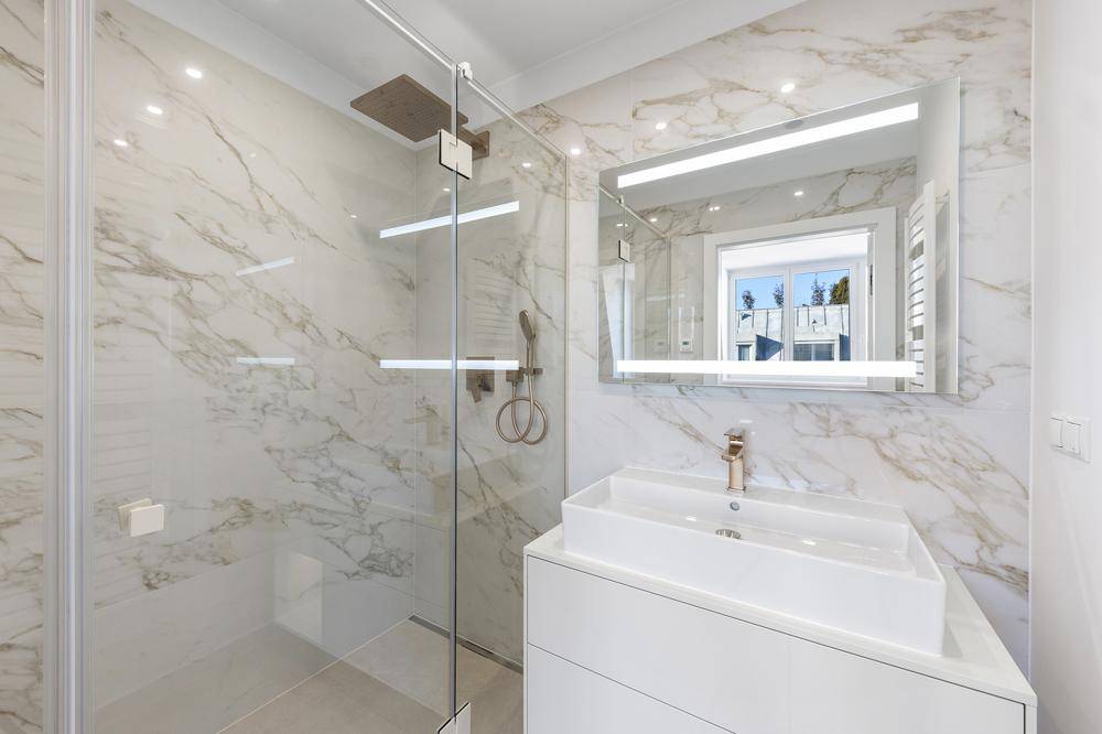Modernes Badezimmer mit Marmorfliesen, begehbarer Dusche und beleuchtetem Spiegel.