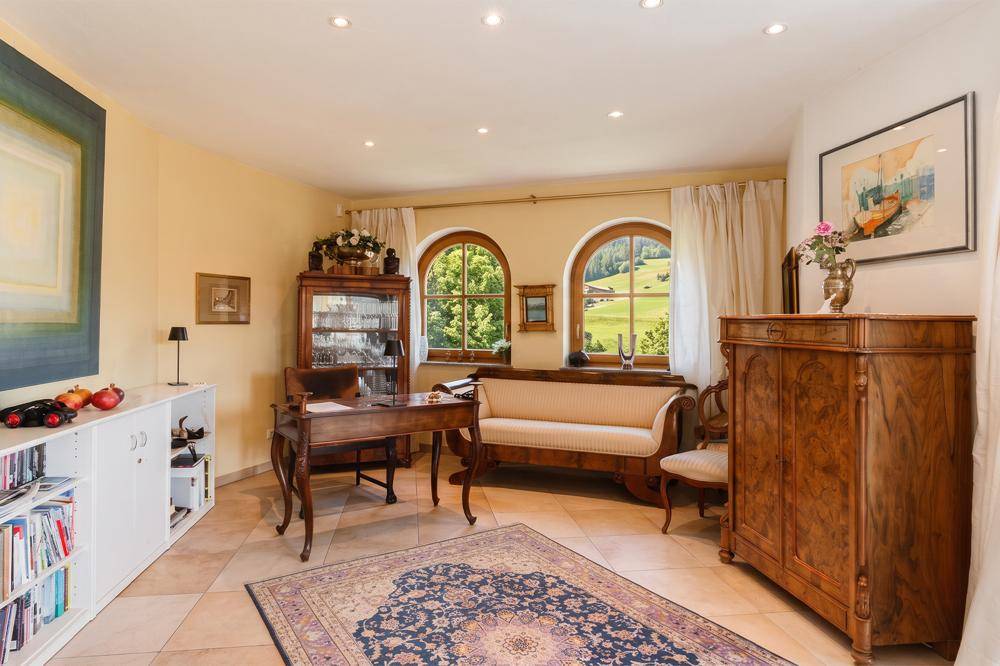 Gemütliches Arbeitszimmer mit antiken Holzmöbeln, Fliesenboden und Rundbogenfenstern mit grüner Aussicht.