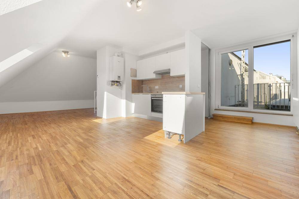 Offener Wohnbereich im Dachgeschoss mit Küchenzeile, Holzfußboden und Zugang zur Terrasse.