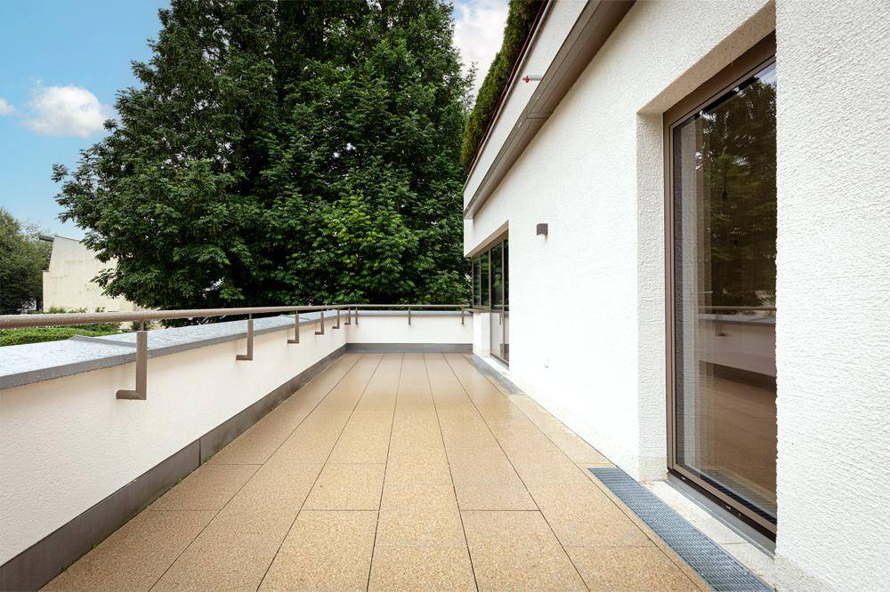 Geräumiger Balkon mit Fliesenboden, modernem Geländer und Blick ins Grüne.